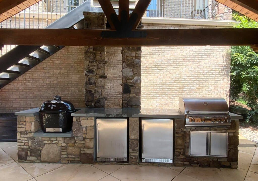 Outdoor kitchen with stone pillars and built-in grill under a covered patio